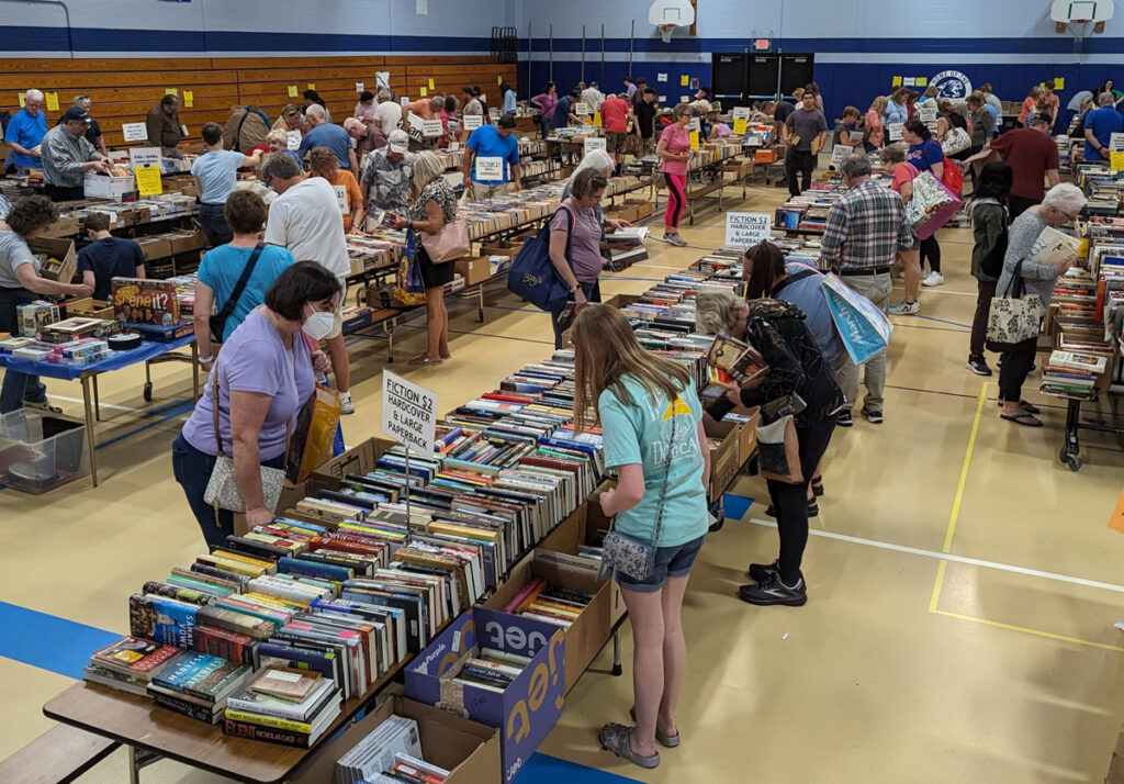 Many people browsing tables full of used books for sale in a school gymnasium
