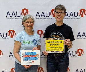 AAUW Naperville Area (IL) 2023 Booksale chairs Anne Swanson and Kath Camasto posing in front of a large AAUW banner with signs promoting reading