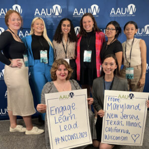 Eight women college students pose in front of an AAUW banner at the 2023 NCCWSL conference in College Park, Maryland