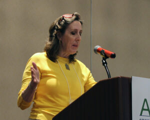 Woman in yellow sweater speaking from a podium