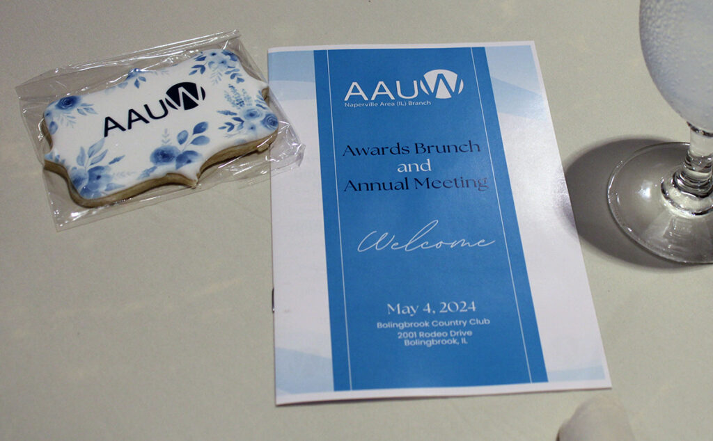 AAUW Awards Brunch and Annual Meeting blue and white program on a table with a cutout cookie decorated with AAUW logo in blue & white icing