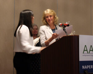 Two women at a podium; one woman holding a certificate