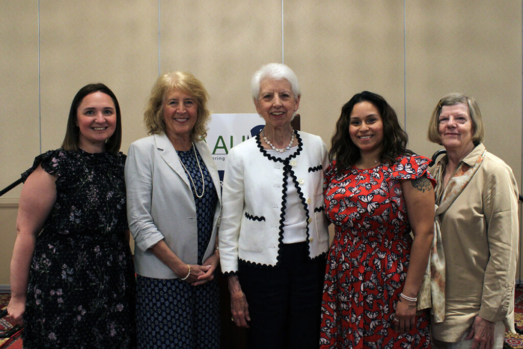 Scholarship recipients Maggie Walsh (left) and Diana Rangel (second from right) with scholarship committee members Joan Schaeffer, Alice Snelgrove and Marge Marek. Group of 5 women posing in front of a podium.