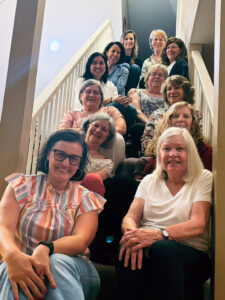 Twelve smiling women sitting on an indoor staircase - members of the AAUW Naperville Area incoming and outgoing board, May 2024