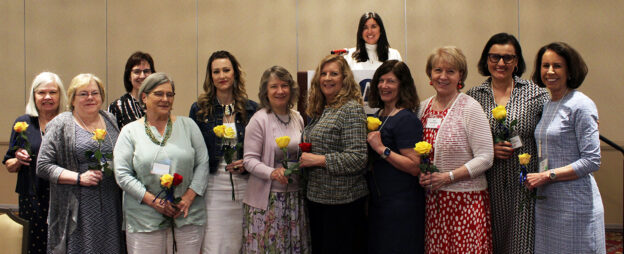 Group of women standing at a podium holding yellow roses at an installation ceremony for incoming AAUW Naperville Area board officers