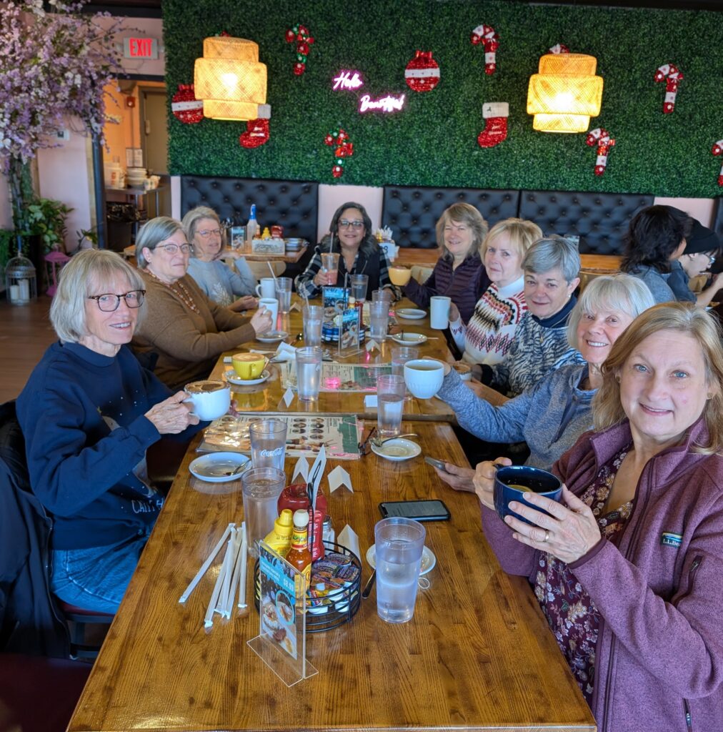 Women dressed casually and holding coffee mugs, sitting around a long restaurant table