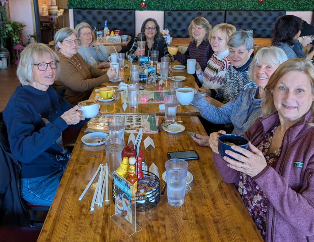 Women dressed casually and holding coffee mugs, sitting around a long restaurant table