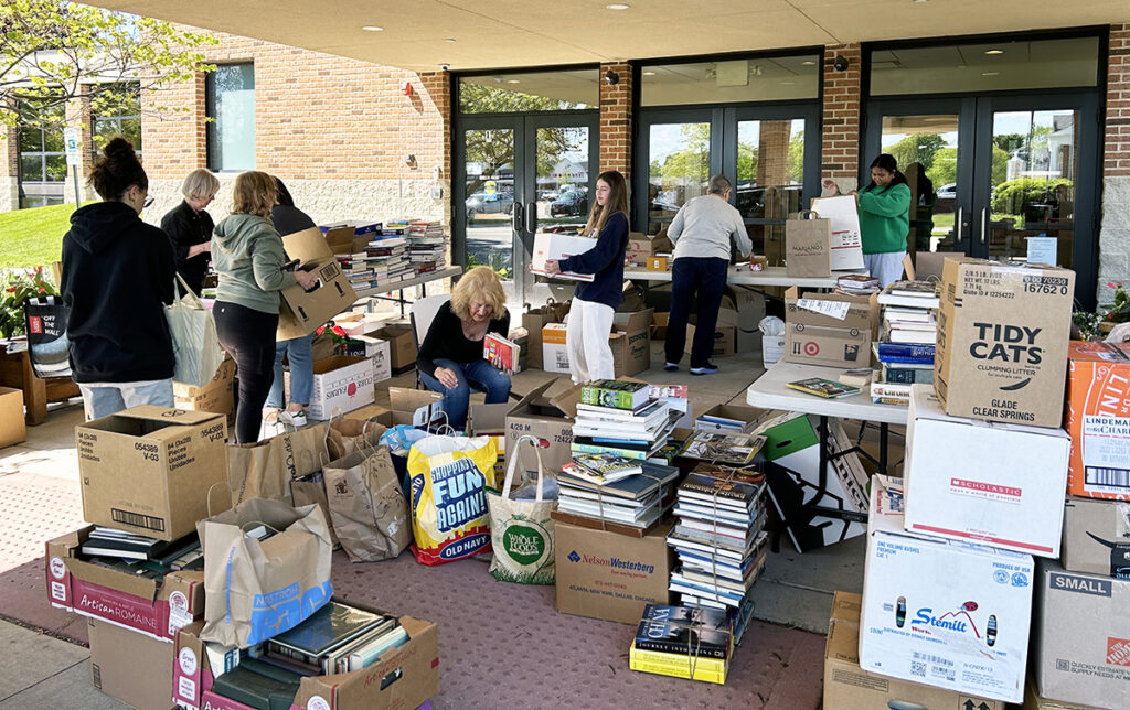 Women collecting and reboxing donated books under the roof of a drivethrough dropoff in front of a building